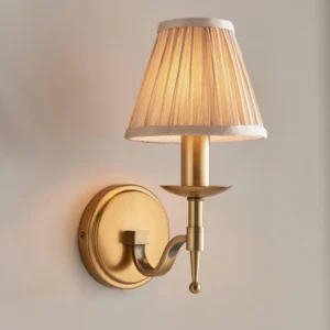 Close-up front view of Baylor wall sconce showing round brass wall plate and tapered pleated fabric shade detail