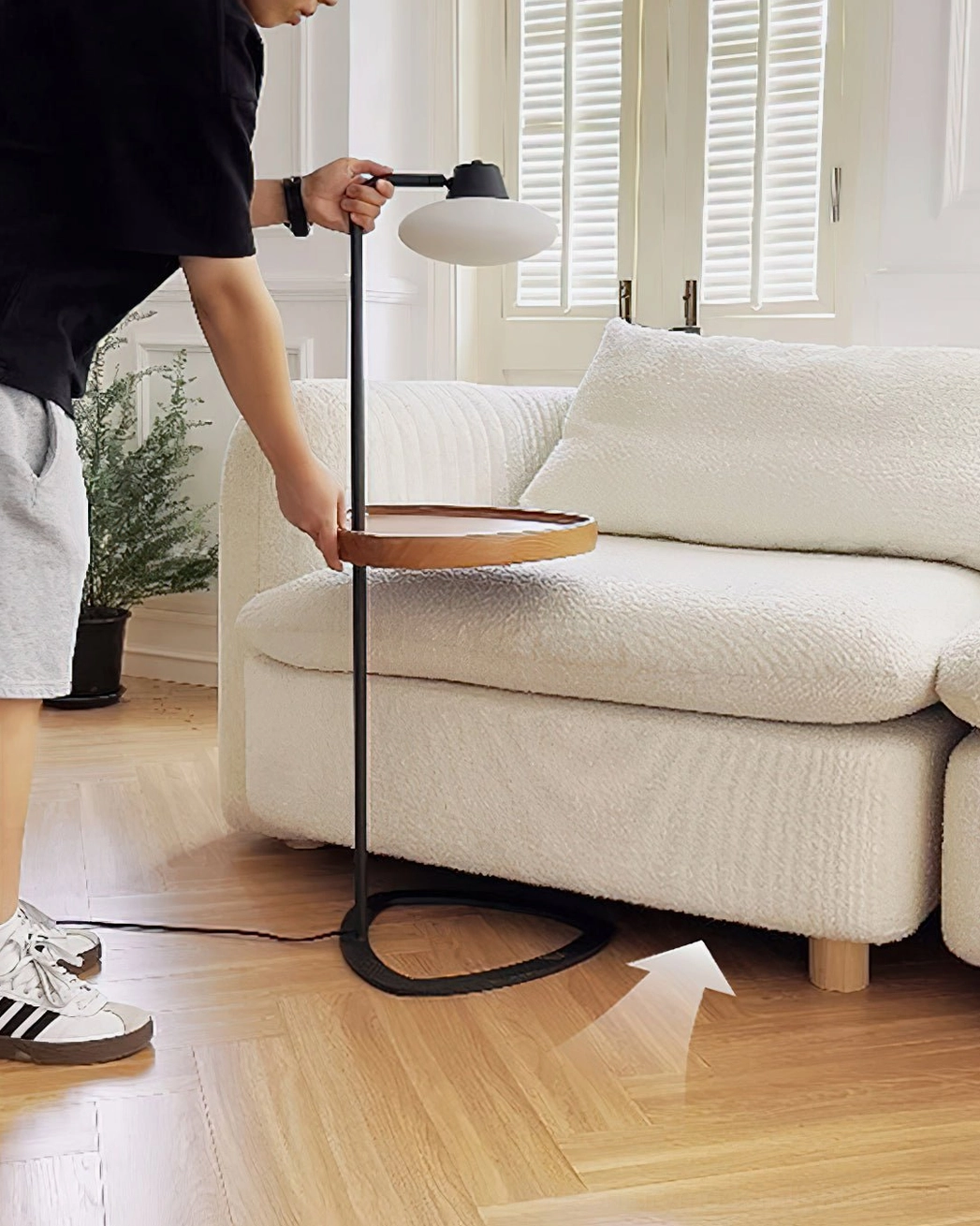 Man adjusting Beatrix floor lamp low-angle view, living room with louvered windows, demonstrates lamp functionality and placement