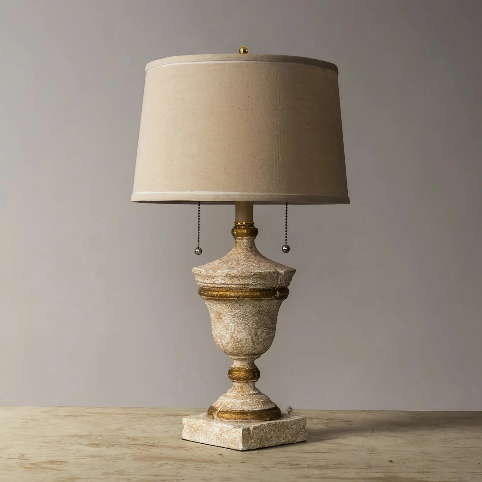 Beatrix vintage table lamp showing distressed antique white finish, beige linen drum shade, and wooden base detailing