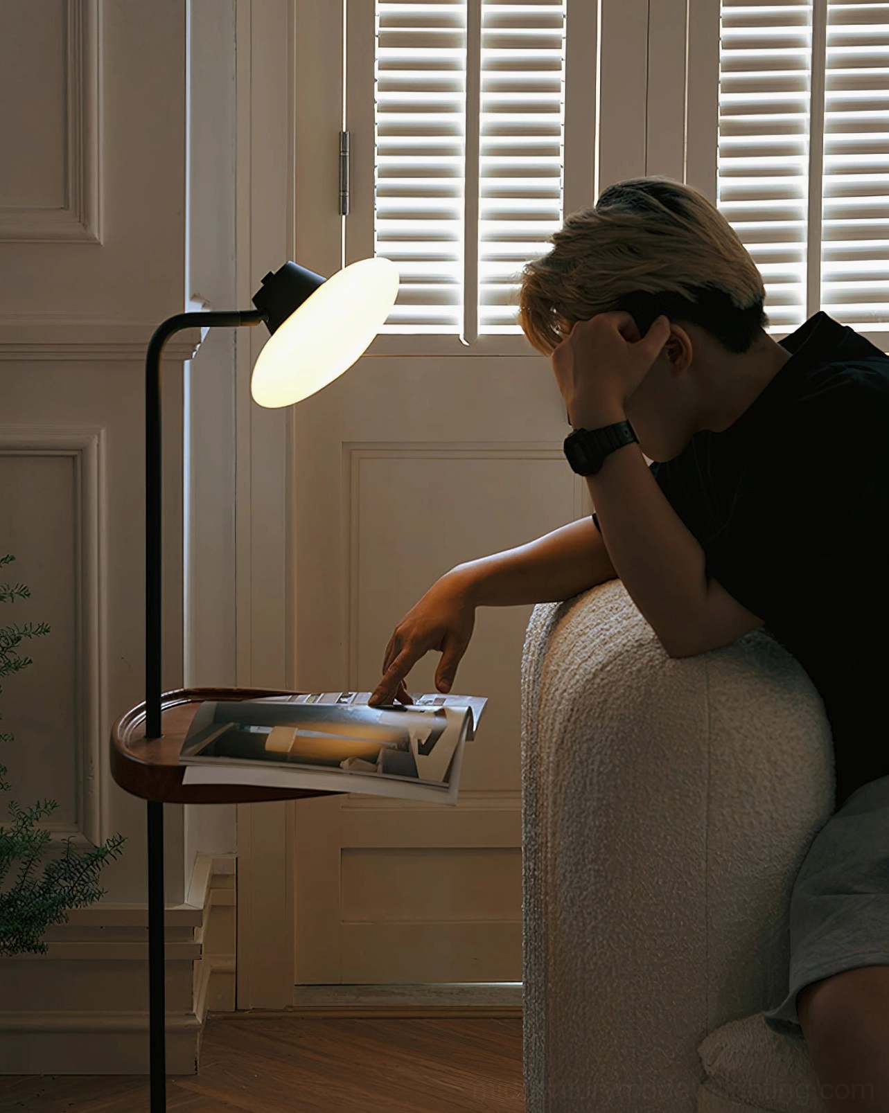 Man reading beside Beatrix floor lamp, low-angle cozy sofa reading area, tray holds magazines and reading materials