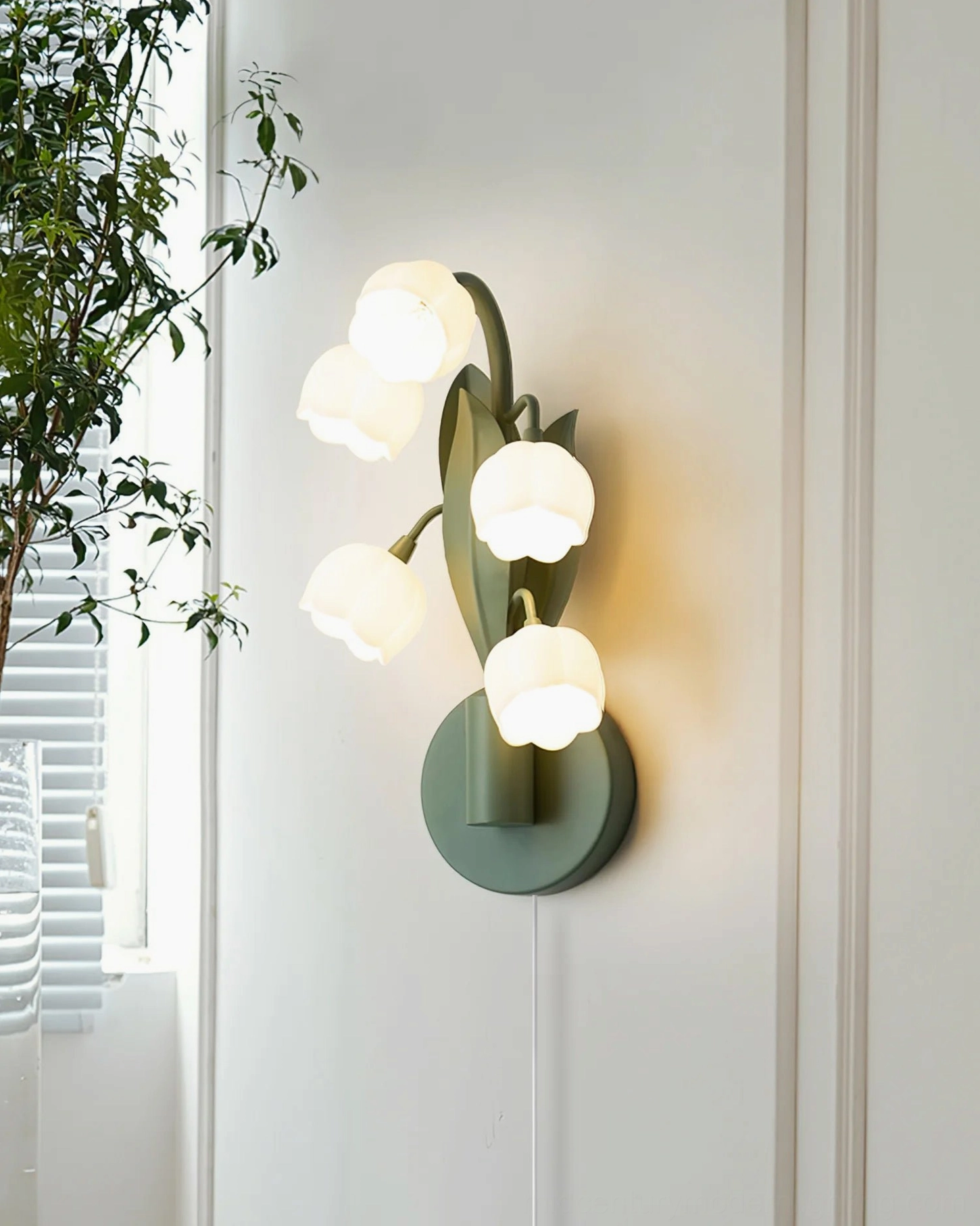 Bell Orchid wall lamp installed in cozy bedroom with window and green foliage, side angle showing five flower heads