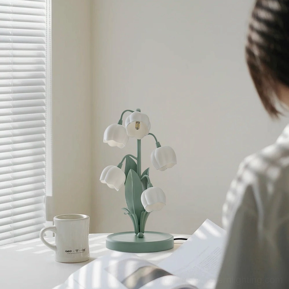 Person at home reading desk with lit Bell Orchid Table Lamp, coffee mug, and open book for task lighting