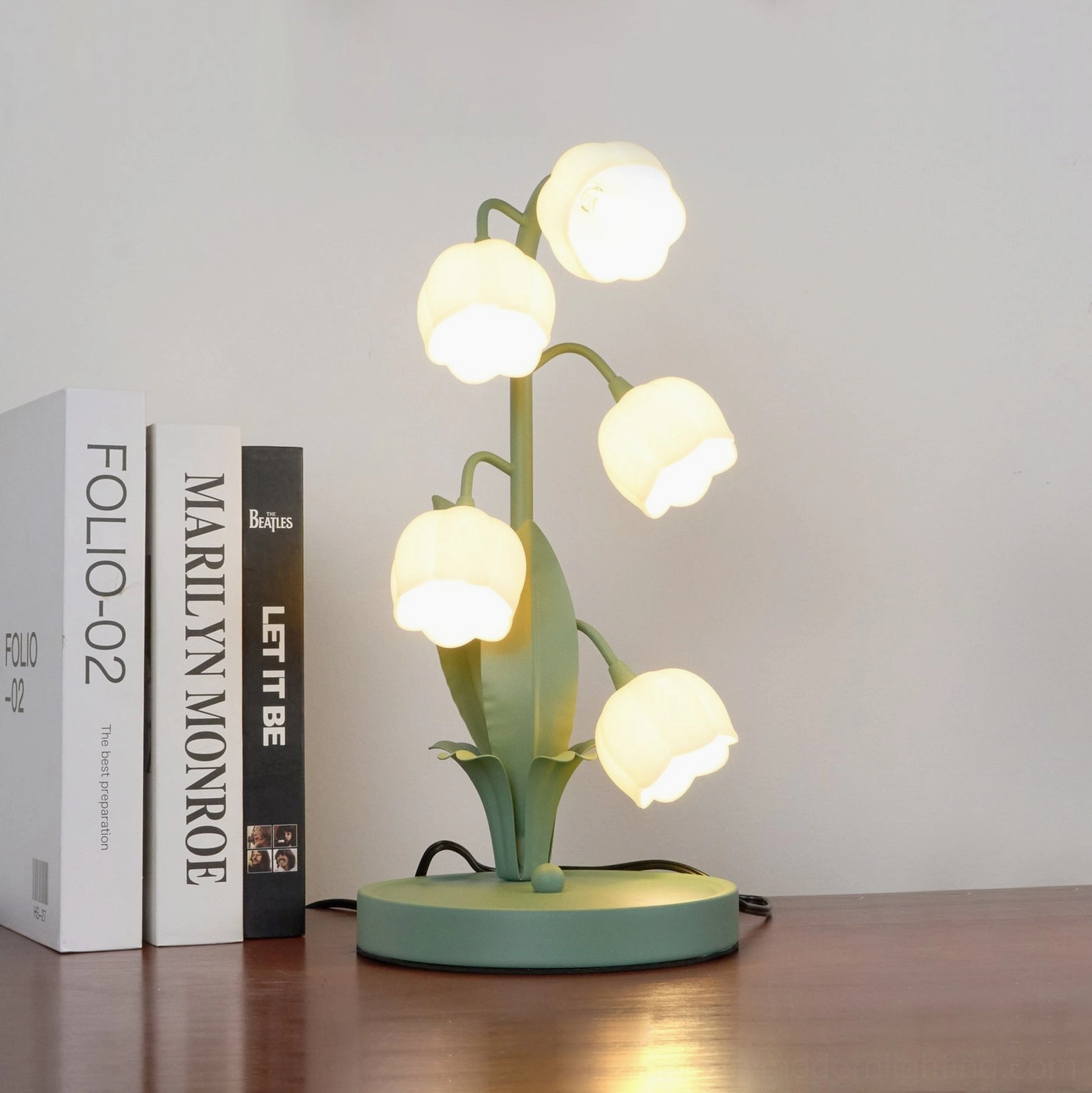 Bell Orchid Table Lamp lit on wooden surface with visible power cord and warm interior lighting aesthetic