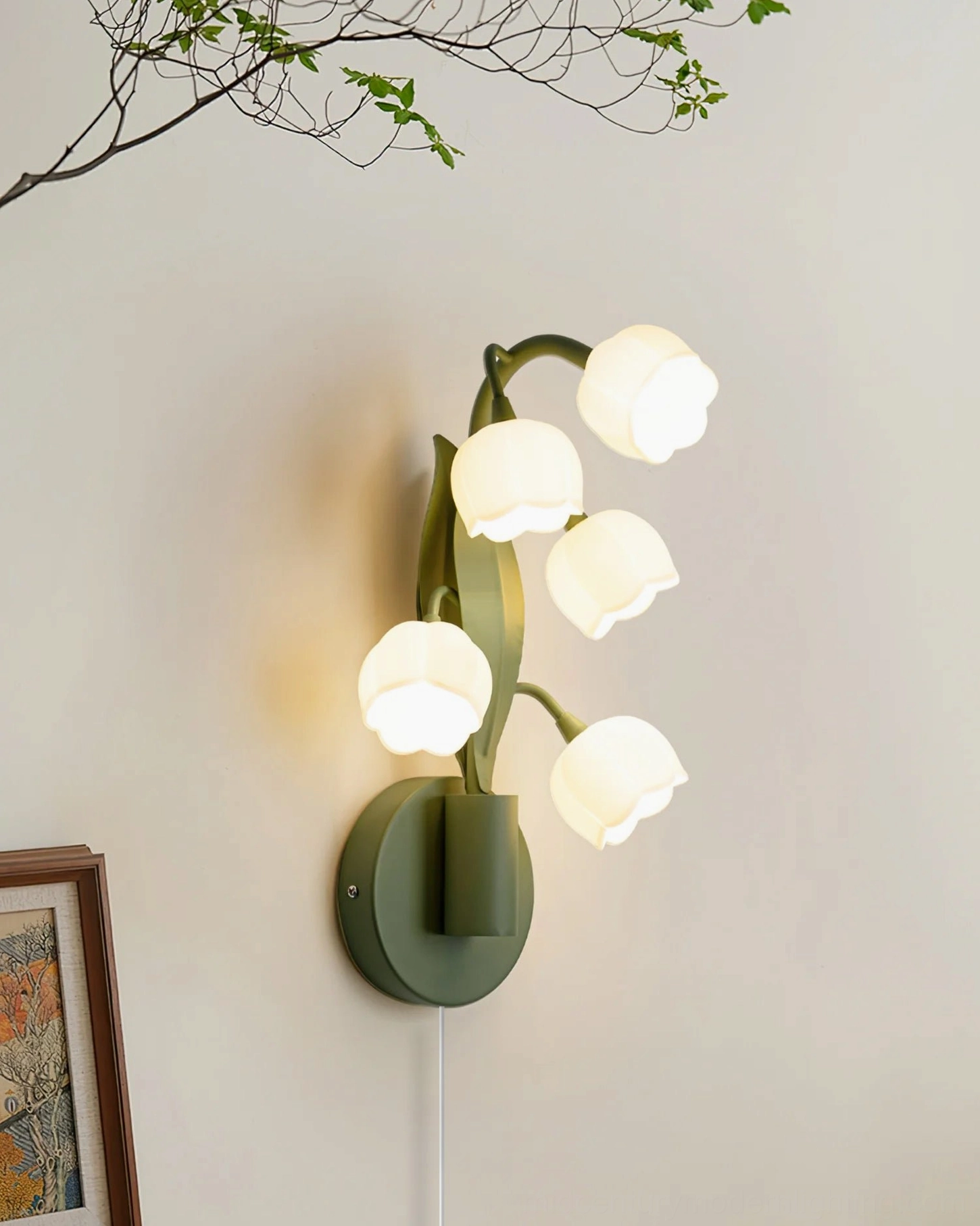 Bell Orchid wall lamp with five bell-shaped shades mounted on plain wall next to decorative branch, side angle view