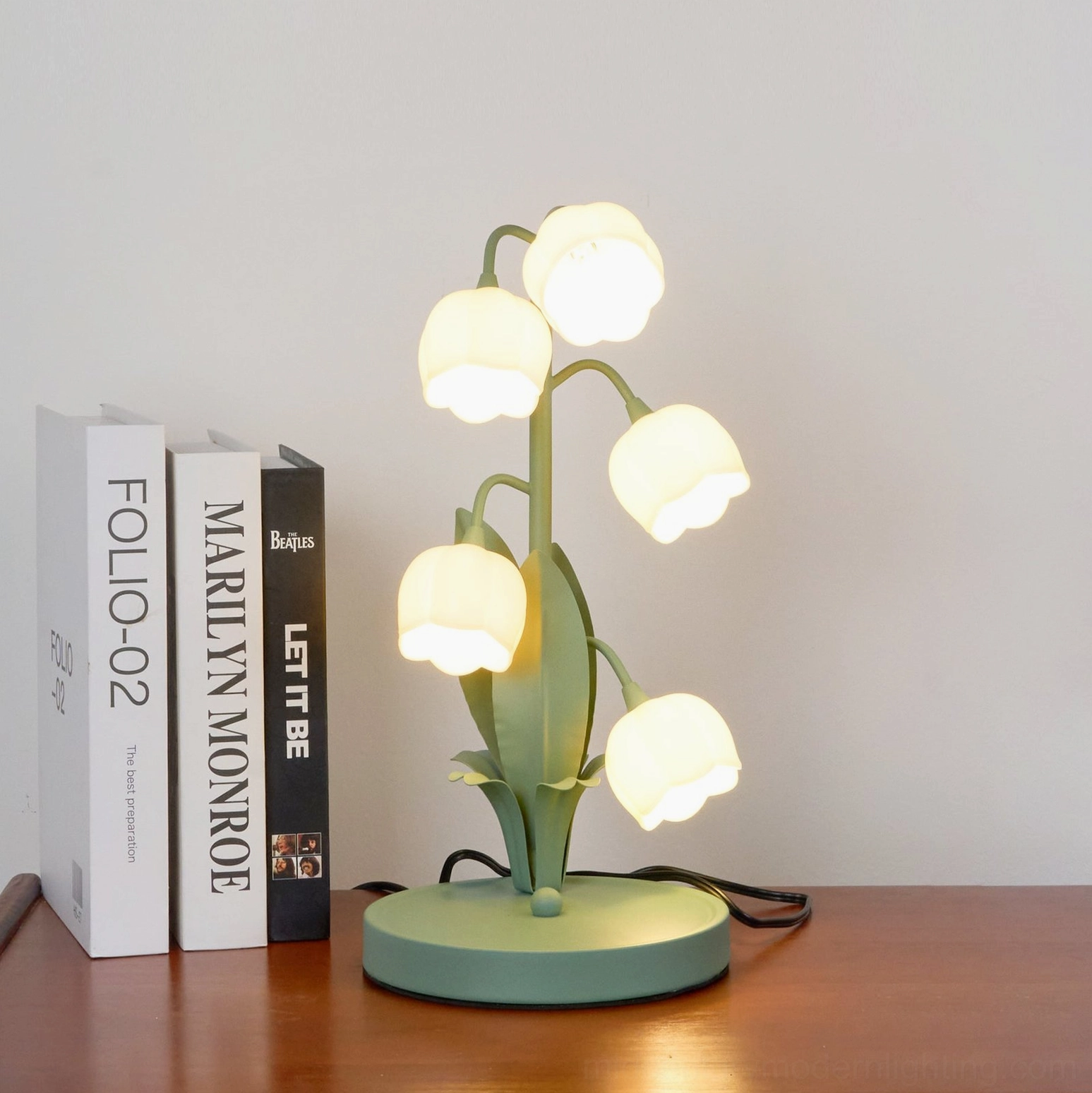 Warm glowing Bell Orchid Table Lamp on wooden desk with book collection and natural lighting ambiance