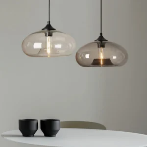 Two Bella glass pendant lights with clear shades hanging above white minimalist dining table, Scandinavian modern interior