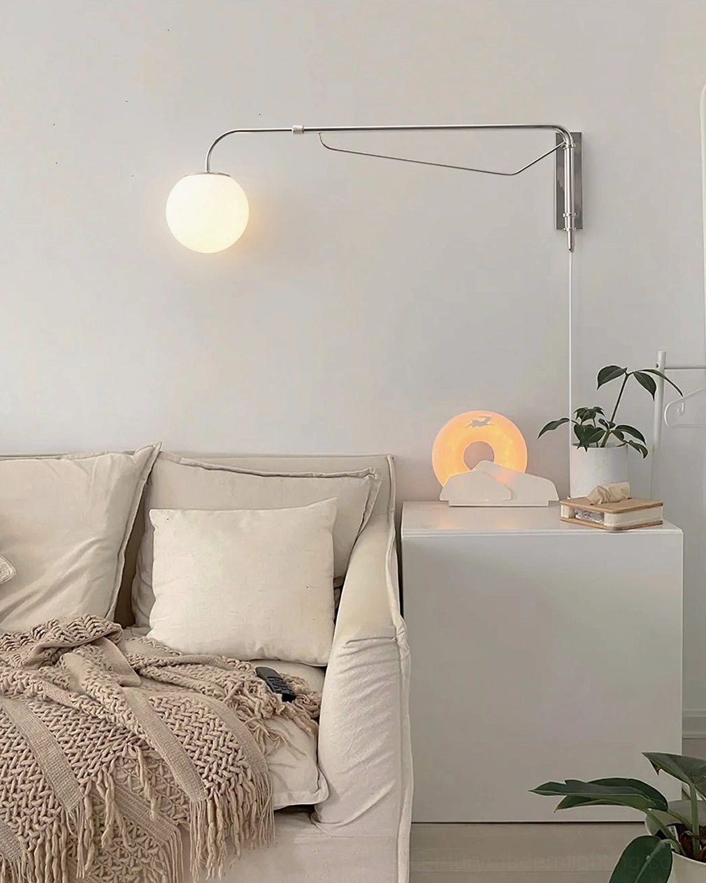 Adjustable arm wall lamp beside living room sofa with accent table and green plant decor