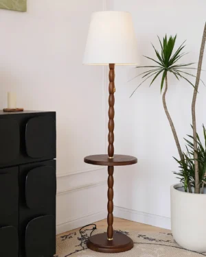 Mid-century floor lamp with side table in living room corner, paired with black cabinet and potted palm plant