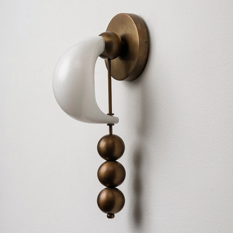 Close-up bent glass wall sconce with antique brass metal framework and three spherical pendants, milky white crescent glass shade