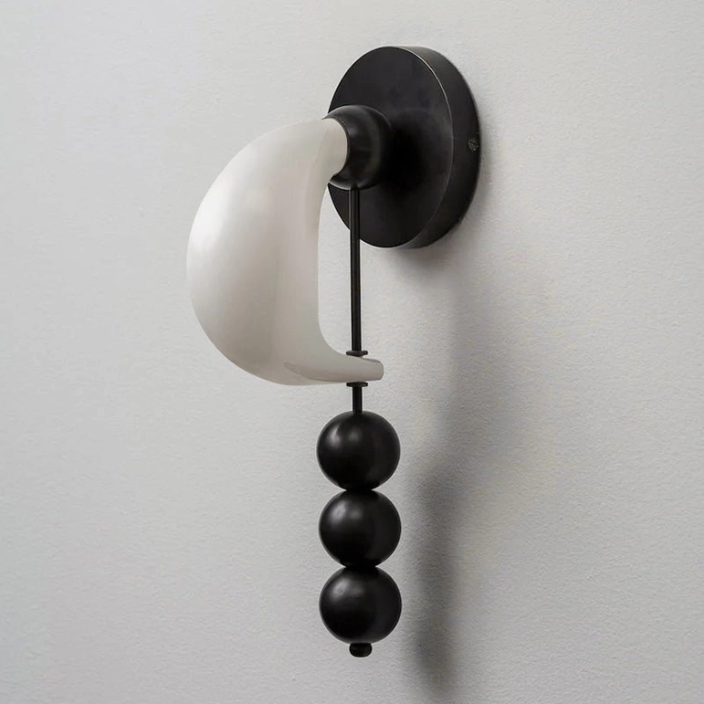 Bent glass wall sconce with matte black metal base, hand-formed curved glass shade, and sculptural sphere details on gray wall