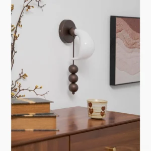 Mid-century modern bent glass wall sconce installed in home study nook with wooden dresser, showing warm ambient lighting and architectural presence