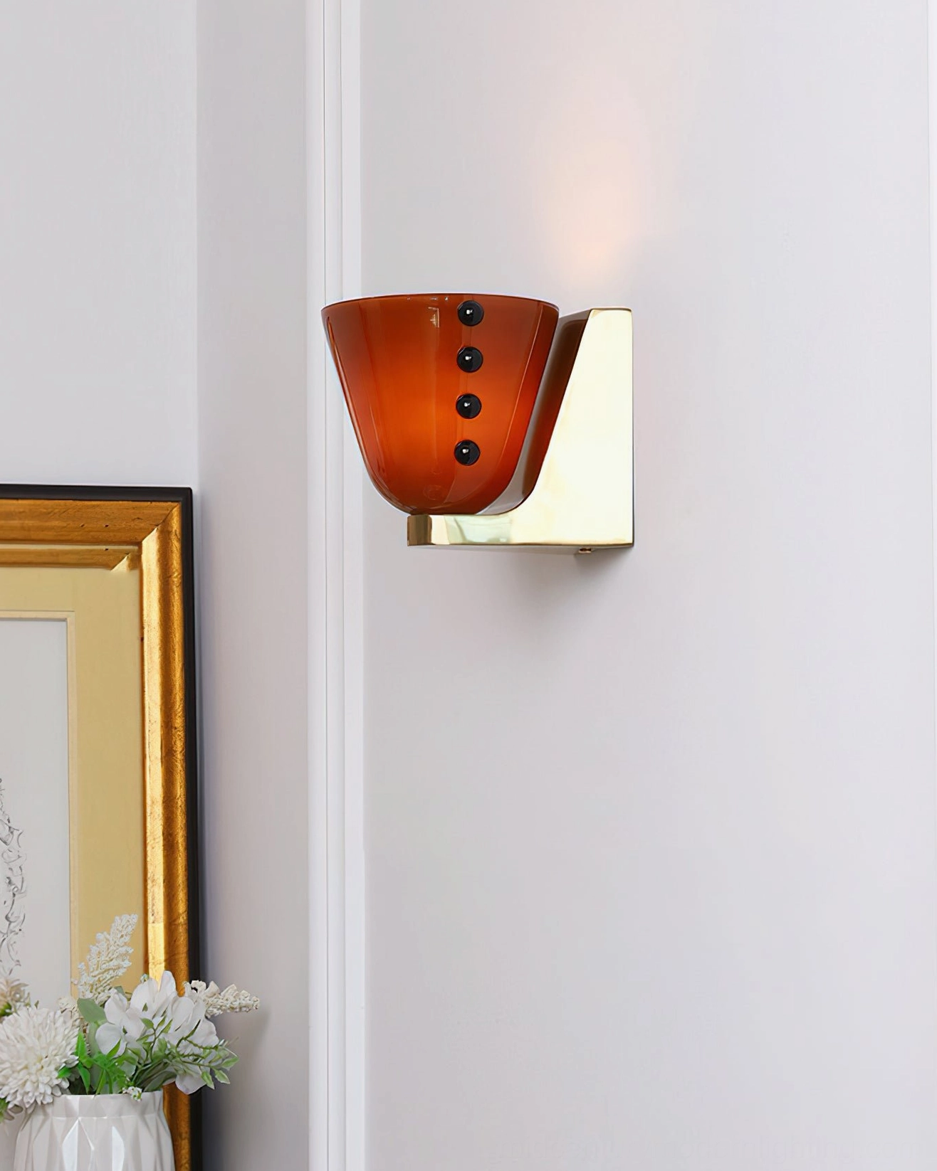 Berries wall lamp with reddish-brown glass shade and brass base in home hallway with framed wall decor