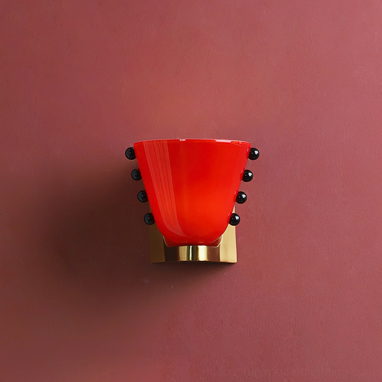 Berries wall sconce with bold bright red glass shade, multiple black bead accents, and brass gold base on burgundy wall