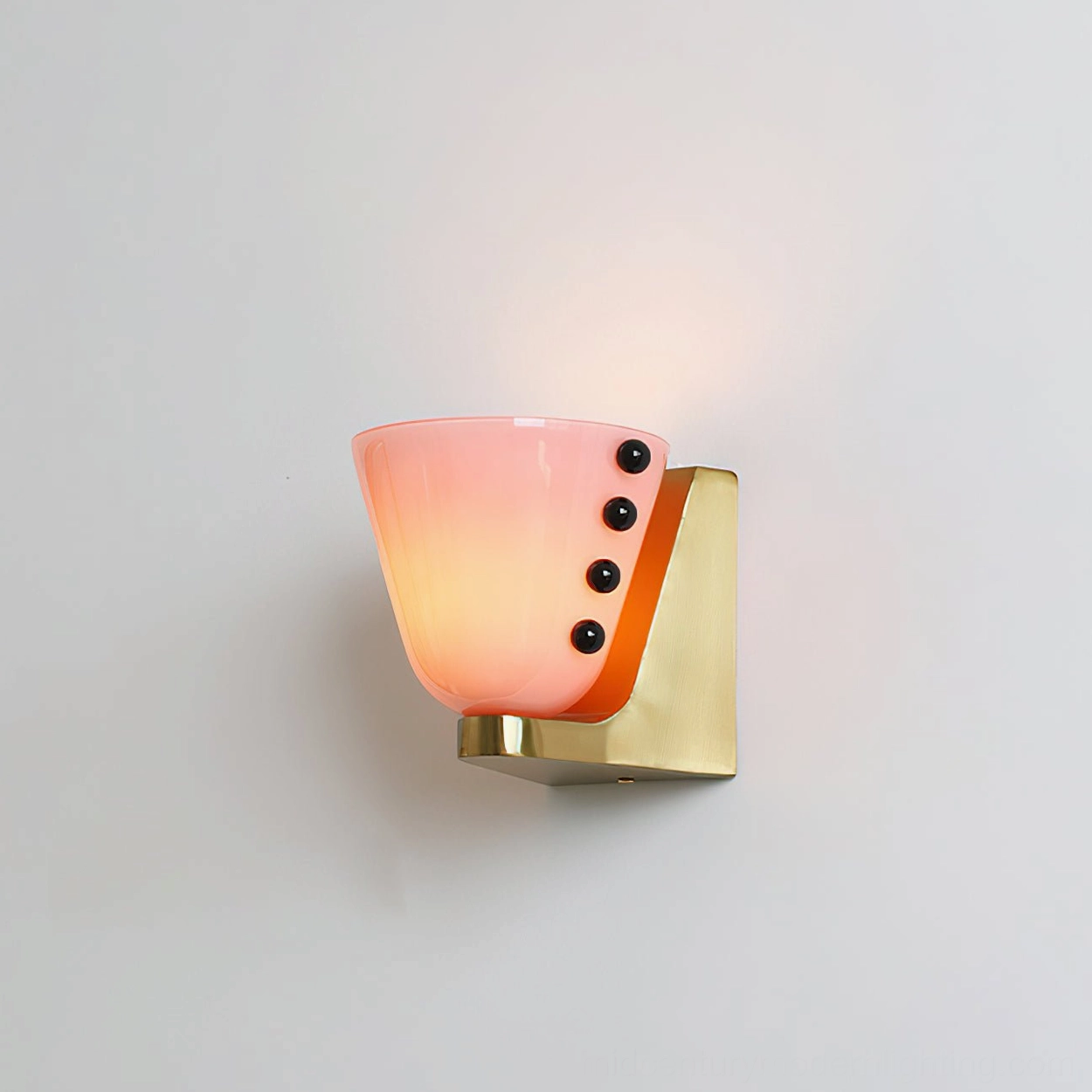 Lit Berries wall sconce with pale pink frosted glass diffusing warm glowing light, brass-finished base components