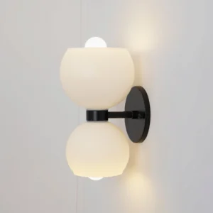 Betty mid-century wall lamp mounted on plain white wall, side perspective showing matte white glass shades and black metal bracket with warm lighting