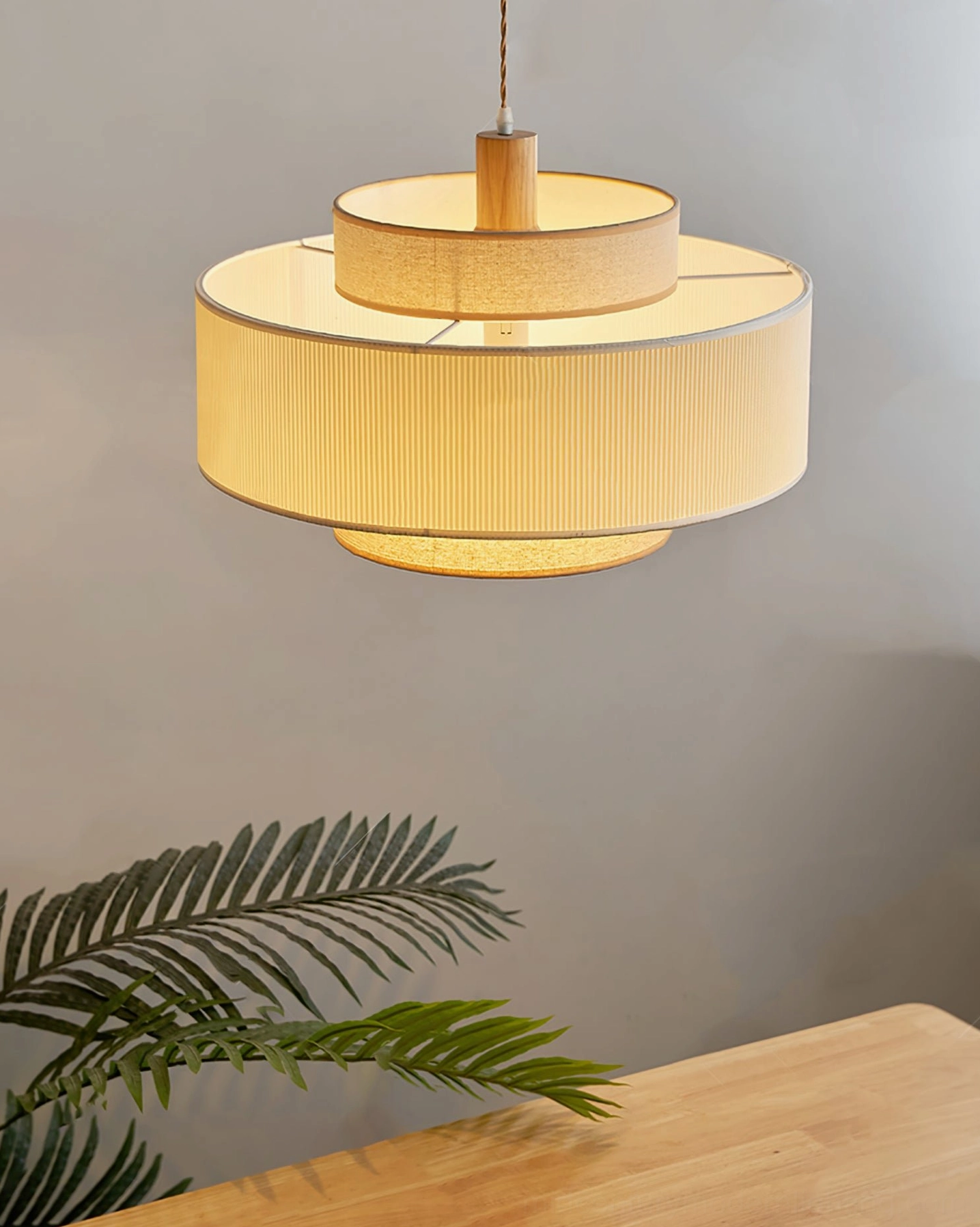 Illuminated Bianella pendant lamp emitting warm yellow glow, pleated beige shade creating soft light diffusion