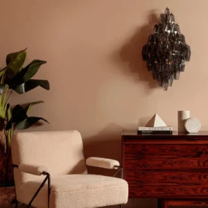 Dark smoky grey polyhedral glass sconce installed in minimalist living room with modern décor and boucle chair