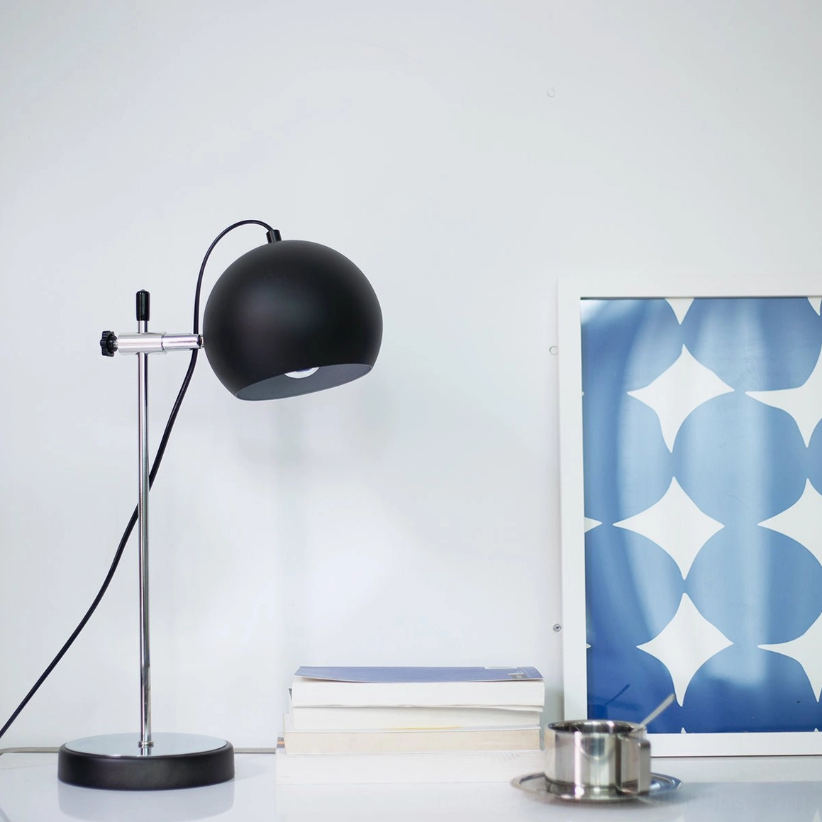 Black matte ball bracket table lamp on minimalist desk with books and wall art