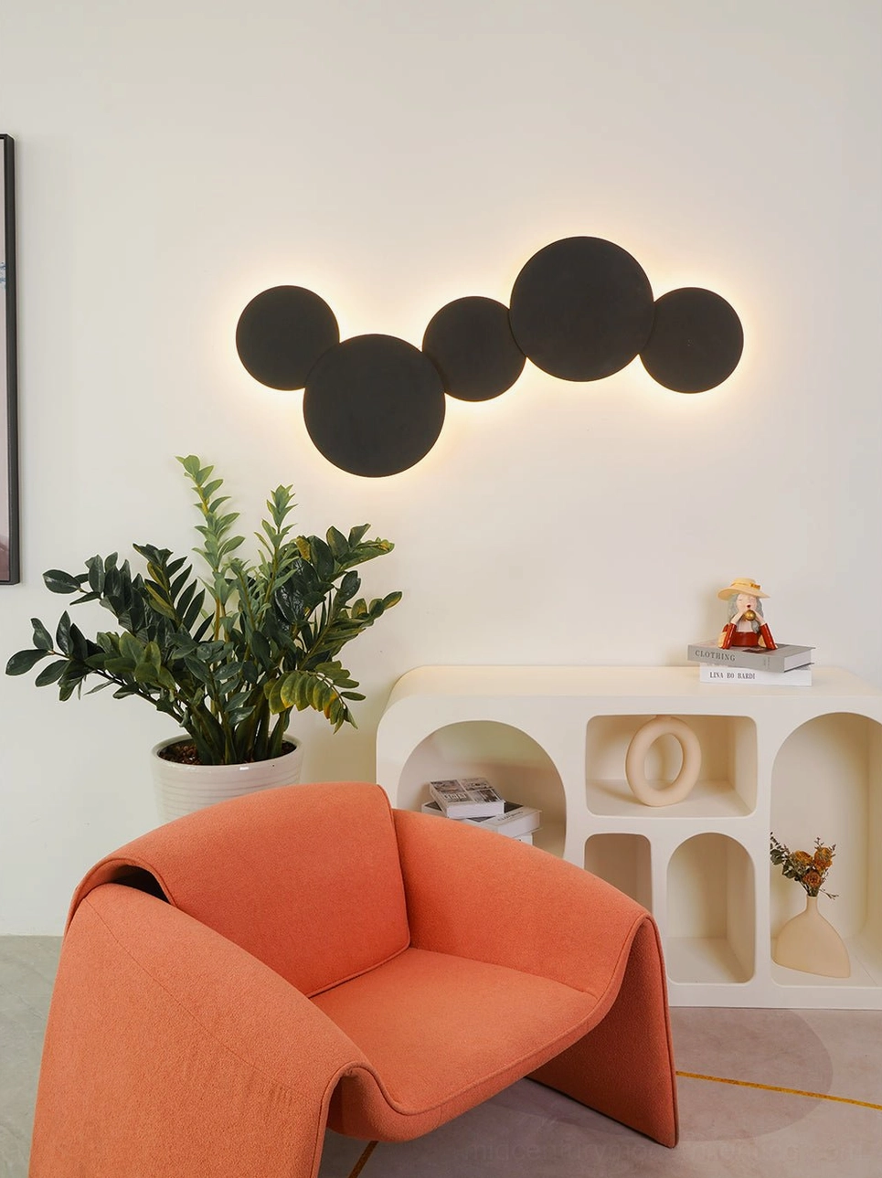Matte black modern geometric disc wall sconce in minimalist living room with orange armchair and contemporary interior design