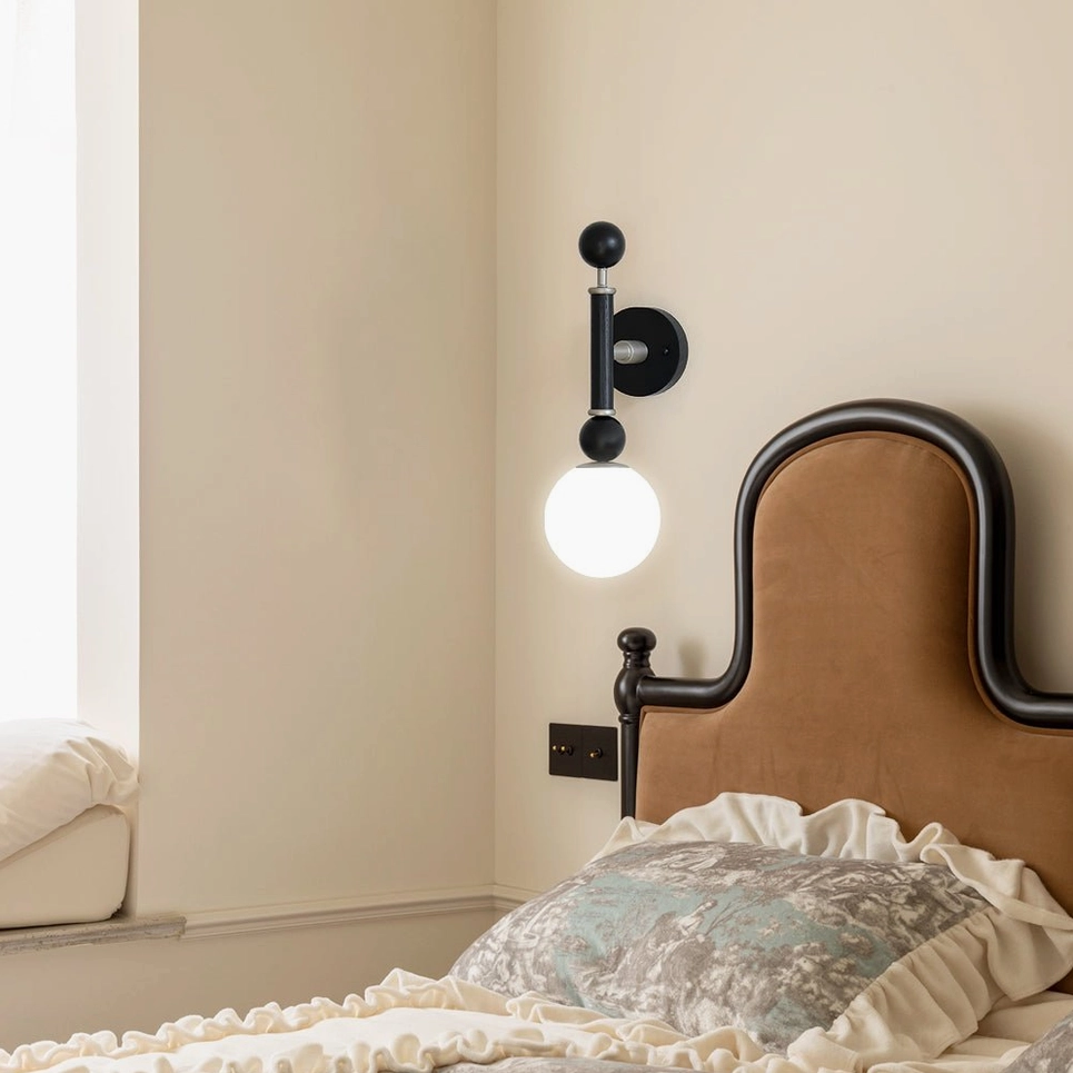 Sculptural black globe wall sconce with silver nickel hardware on white wall background