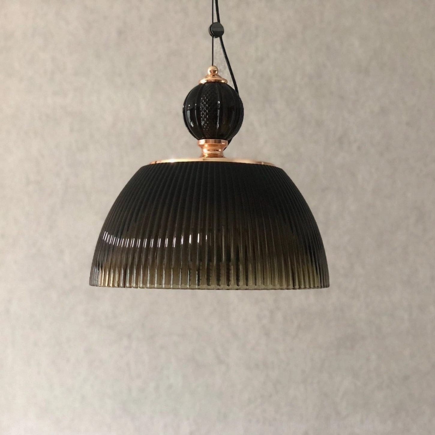 All-black decorated mid-century modern pendant lamp with deep ribbed glass dome on beige textured background