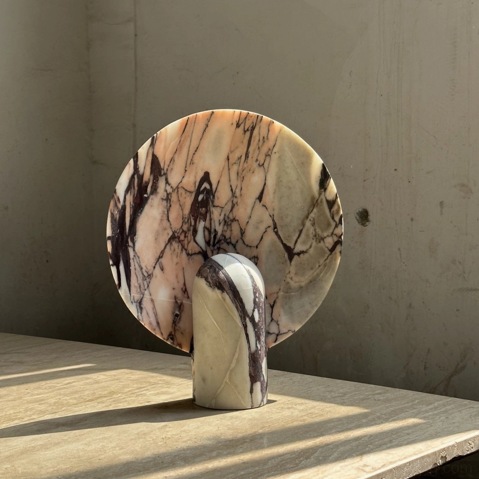 Black and white marble table lamp three-quarter side view on concrete surface with geometric shadow detail, minimalist modern design aesthetic