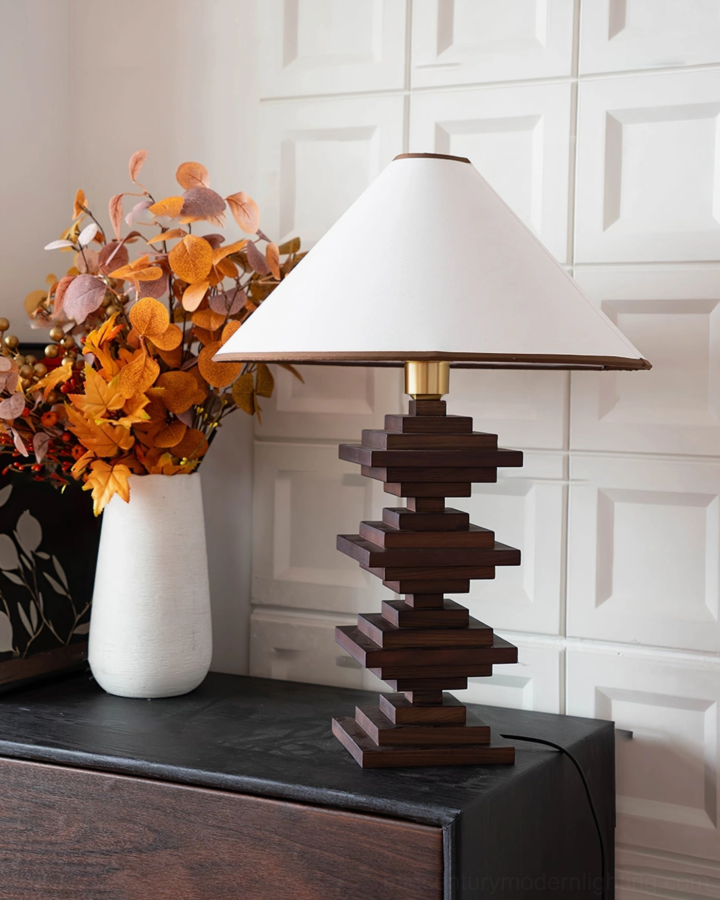 Black stacked wooden tower lamp direct front view on dark wood dresser with white vase