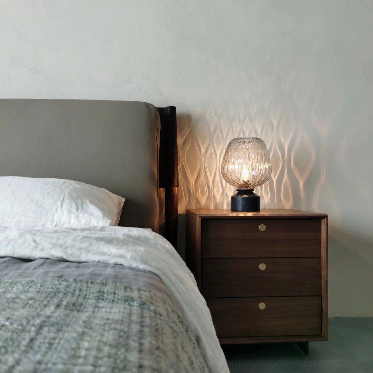 Illuminated blown glass lamp casting rippled light patterns on wooden bedside cabinet in master bedroom