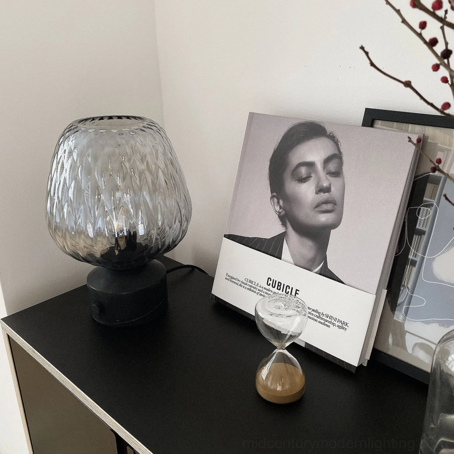 Sculptural glass table lamp on console table with fashion magazine and hourglass décor, sleek modern styling
