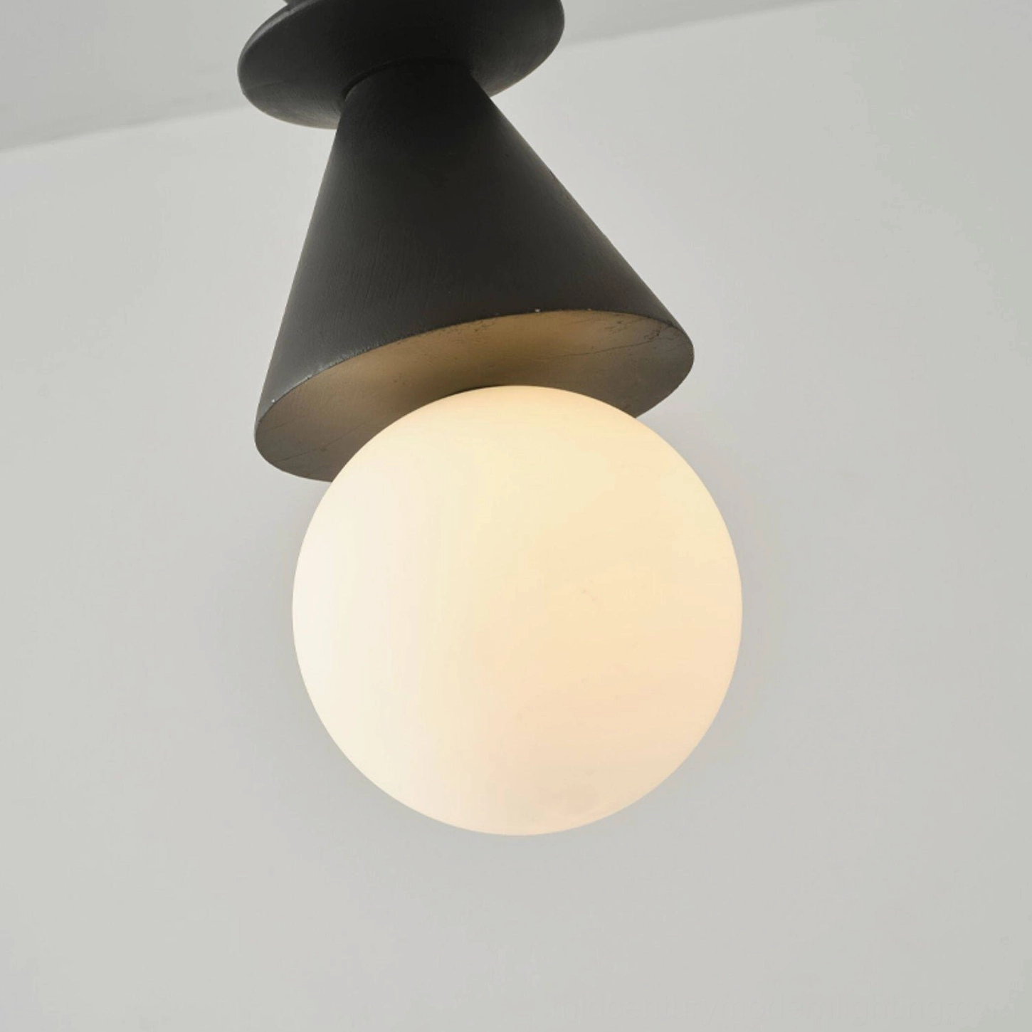 Matte black conical totem pendant light with frosted white globe bulb in close-up studio view on white isolated background