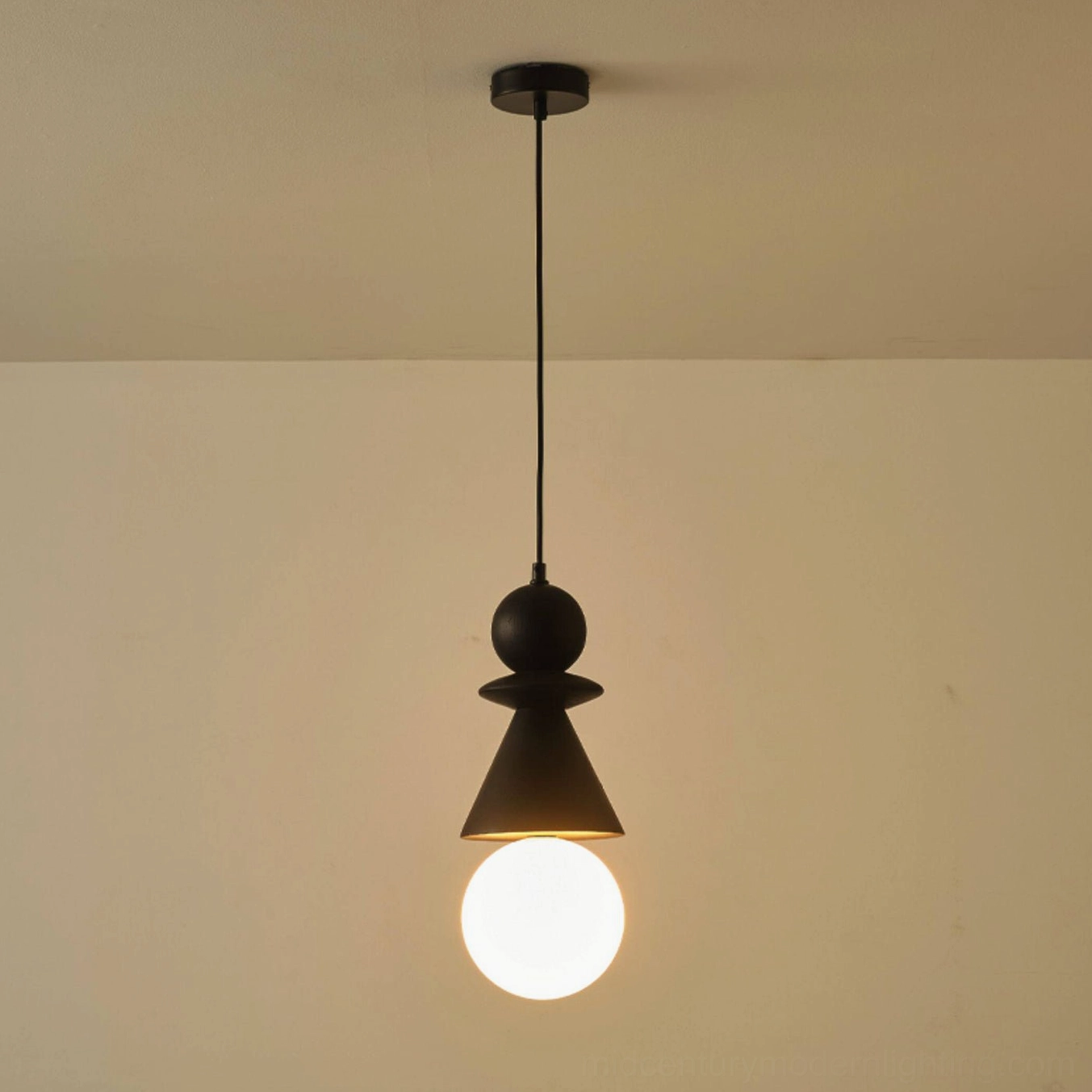 Matte black conical totem pendant light with stacked wood geometry and lit frosted globe against warm beige wall background