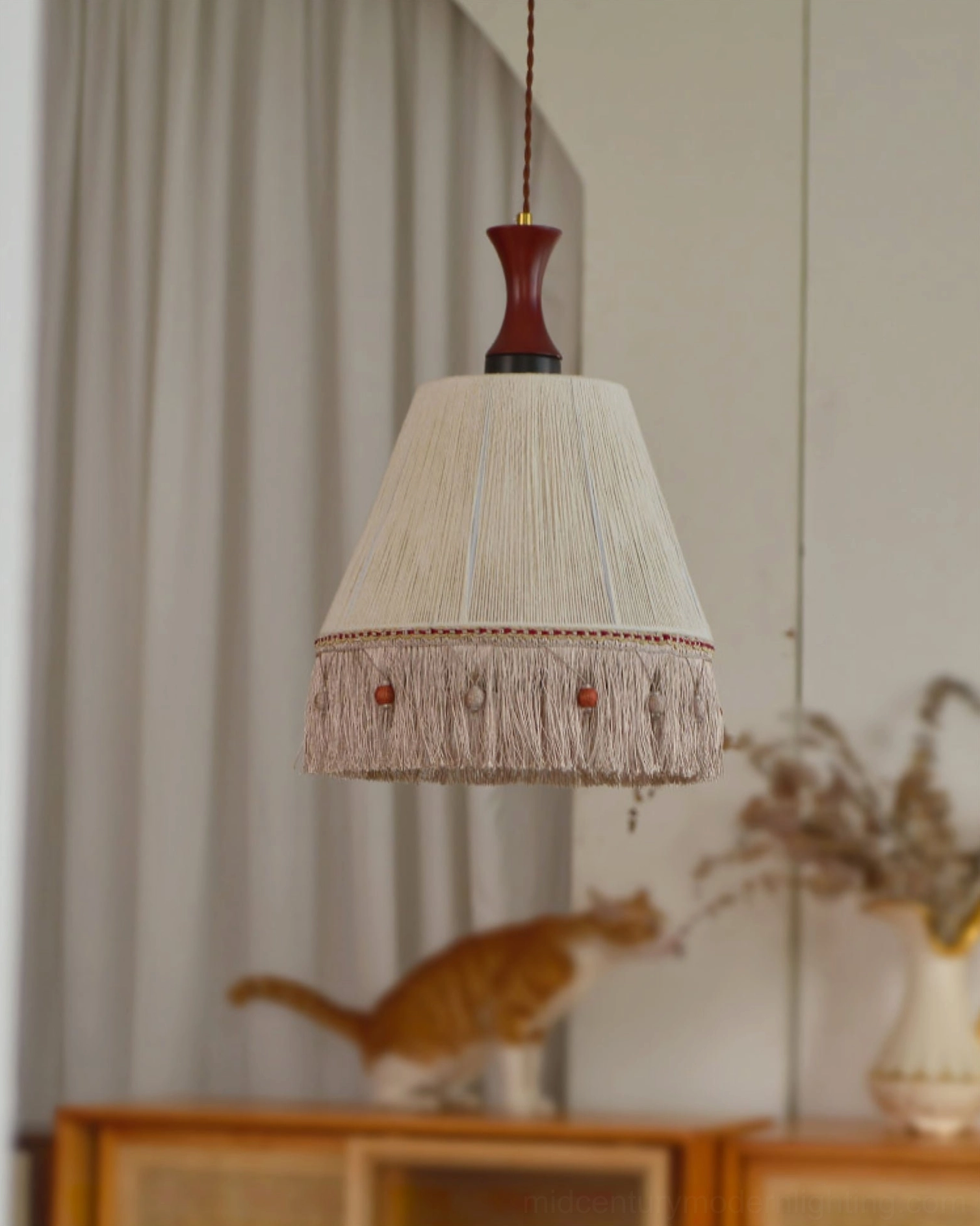 Woven cotton fringe pendant lamp in cozy living room with wooden furniture and dried flowers