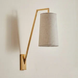 Brass finish Bonny wall light with tapered beige linen lampshade in modern minimalist style, front view on off-white wall