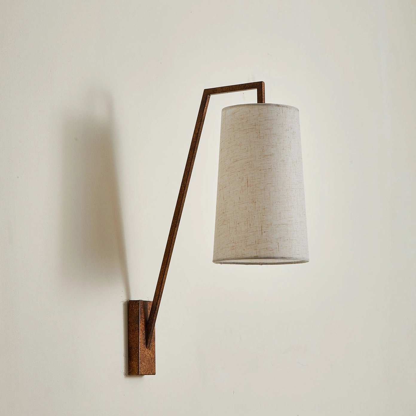Bonny wall sconce with rustic textured brown metal arm, warm beige fabric shade on neutral background, understated elegant styling
