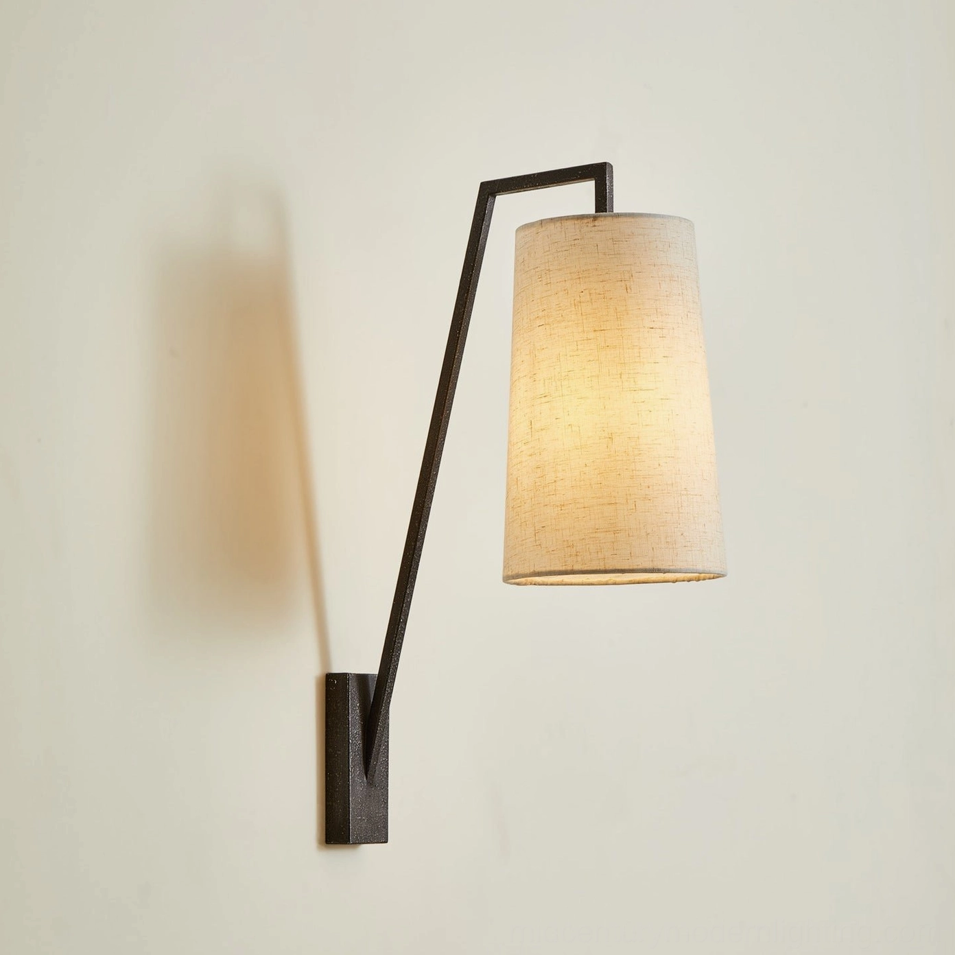 Bonny wall reading lamp illuminated with warm glow, black metal arm and soft beige shade providing ambient lighting on neutral wall