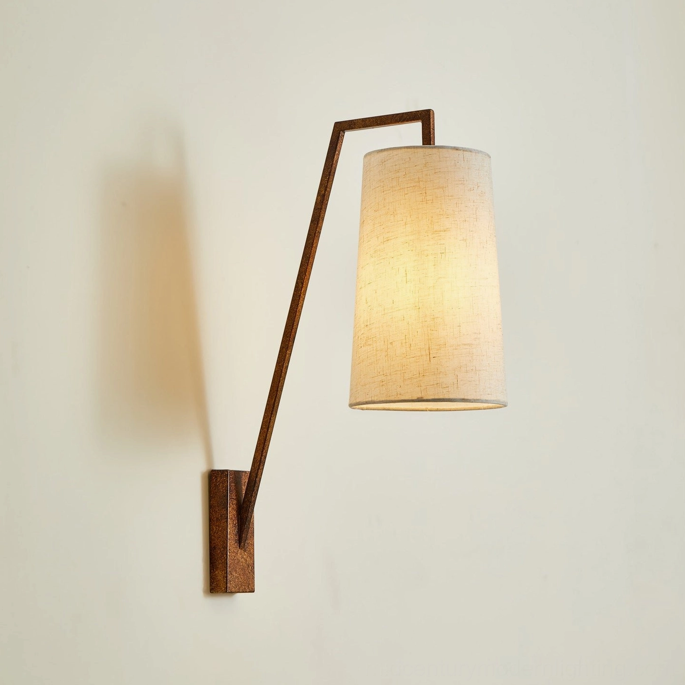 Bonny wall sconce warm lit demonstration with brown metal frame and illuminated beige linen shade creating soft ambient lighting