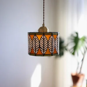 Mid-century modern stained glass leaf pendant light in warm orange and white tones, interior styling with potted plant