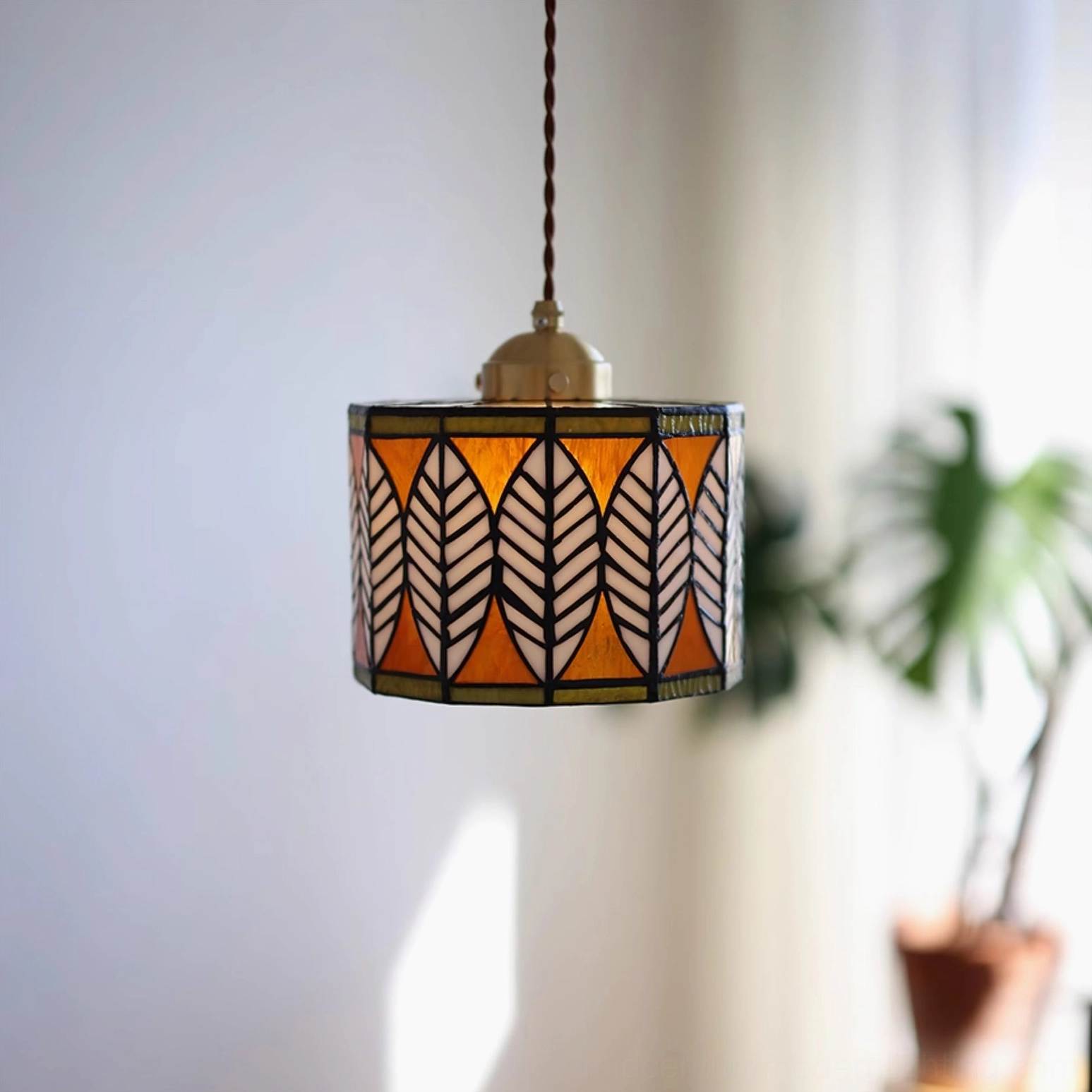 Mid-century modern stained glass leaf pendant light in warm orange and white tones, interior styling with potted plant