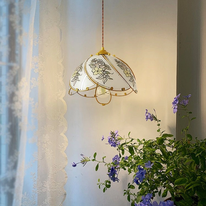 Stained glass lily pendant casting warm light in bright home corner with potted green flowering plants and sheer window curtains