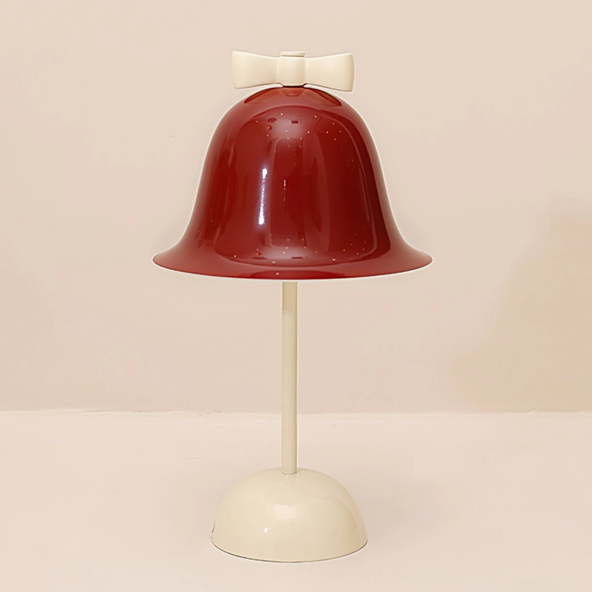 Bow Bell lamp angled three-quarter view displaying sculpted bow detail on top of cream base and bell-shaped red shade
