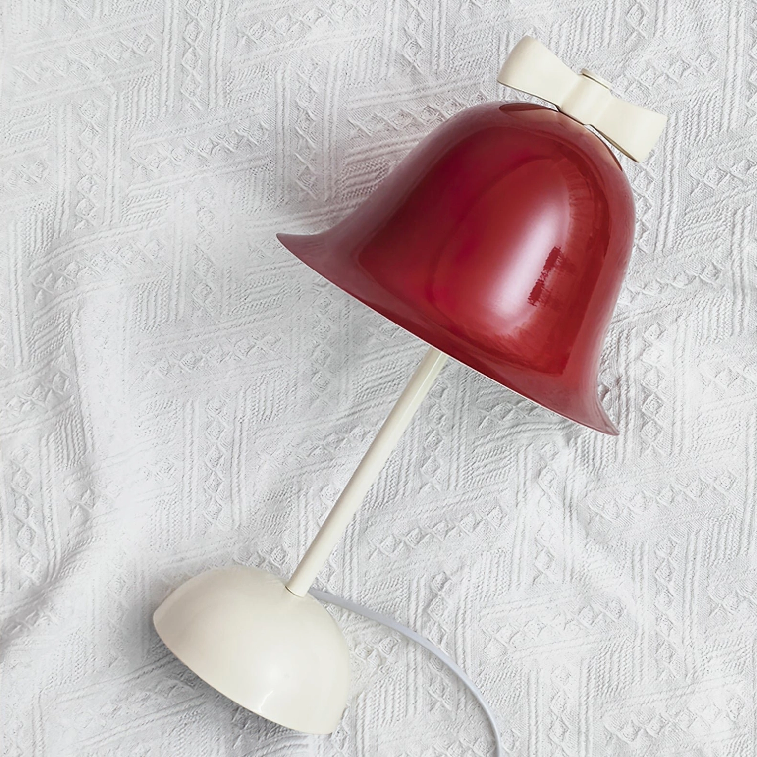 Bow Bell table lamp side profile view lying on white textured fabric surface showing lamp structure and design details