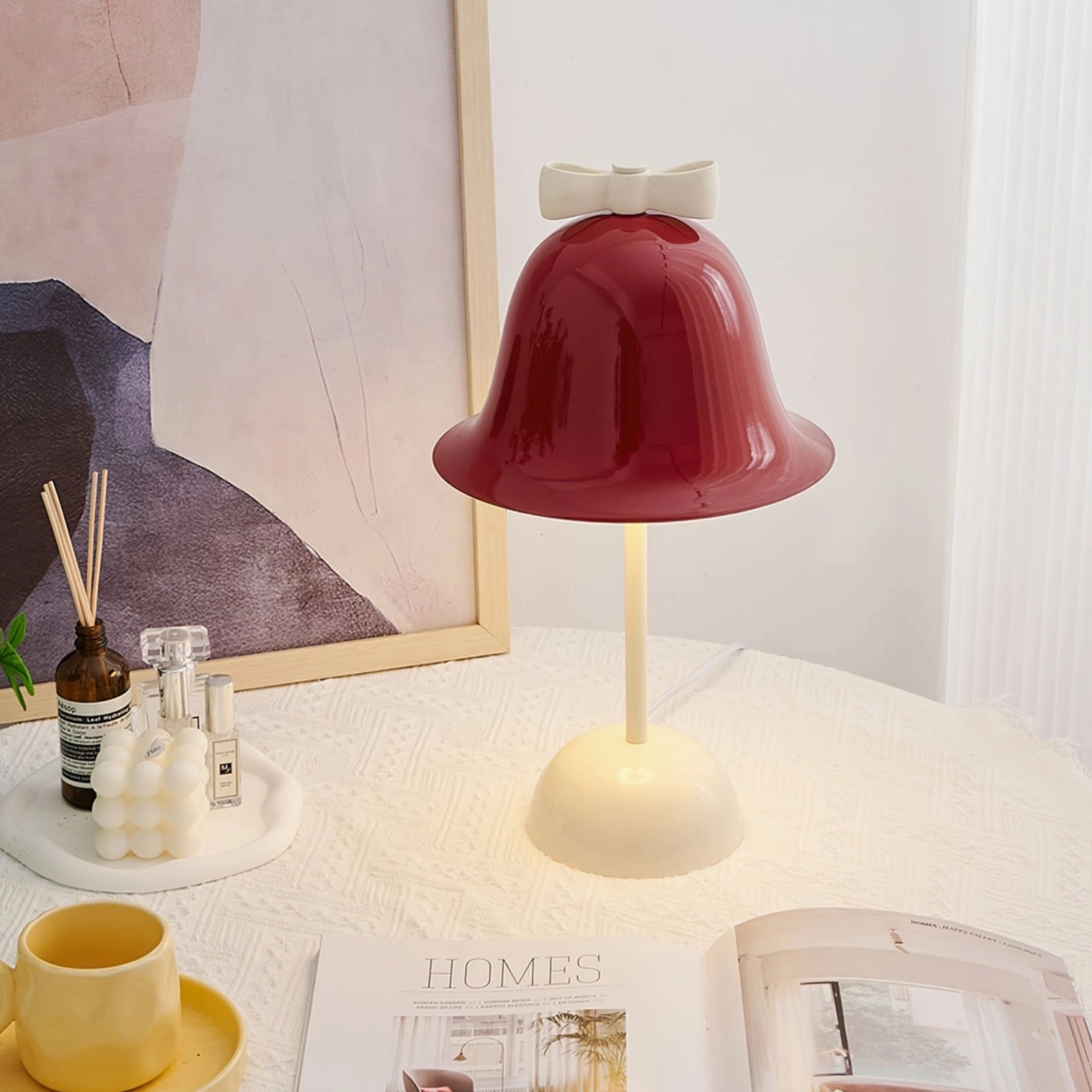 Bow Bell accent lamp on textured white tablecloth with abstract wall art, diffuser, and yellow cup set, lifestyle arrangement
