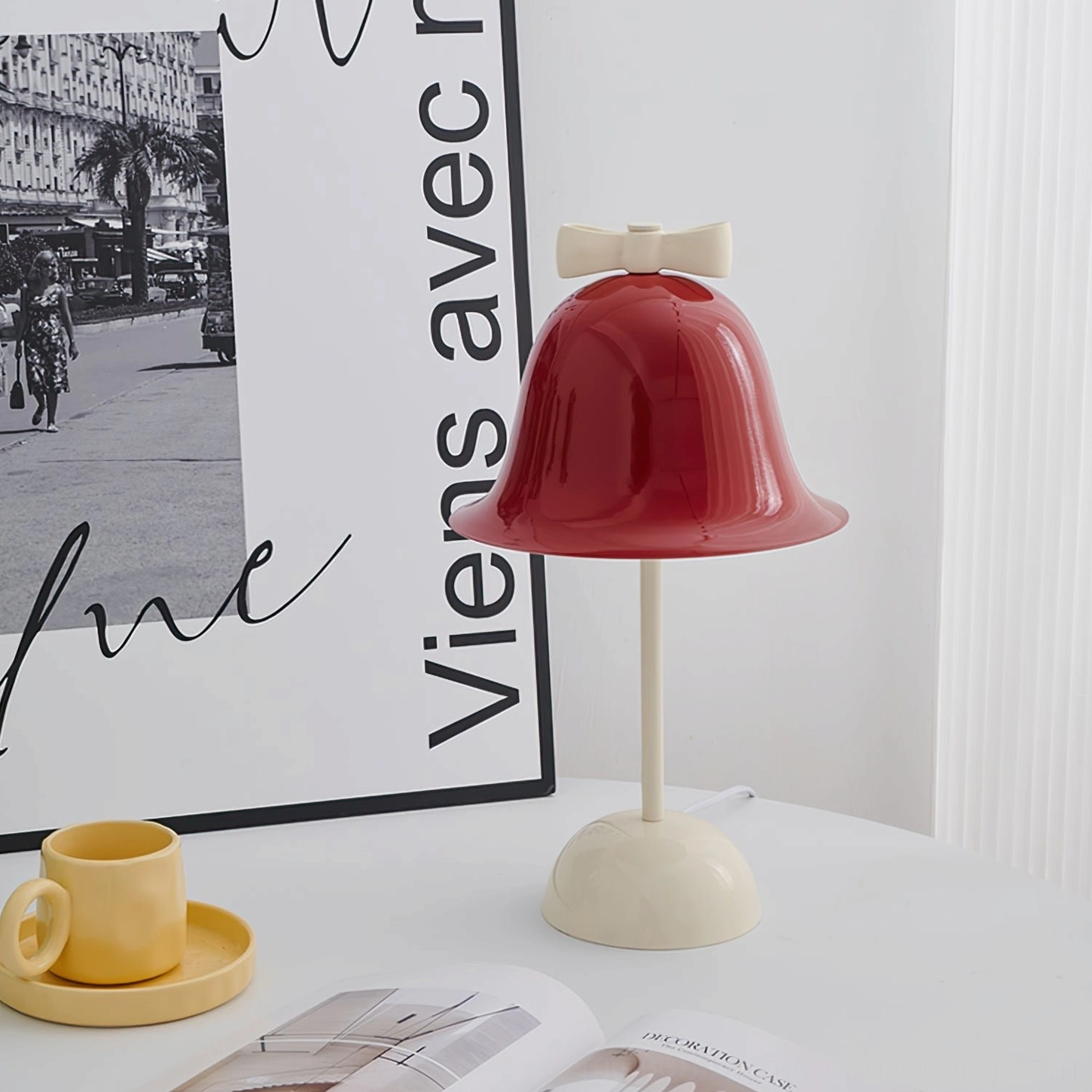 Bow Bell mid-century modern lamp displayed on table with vintage French poster, yellow cup saucer, and home magazines