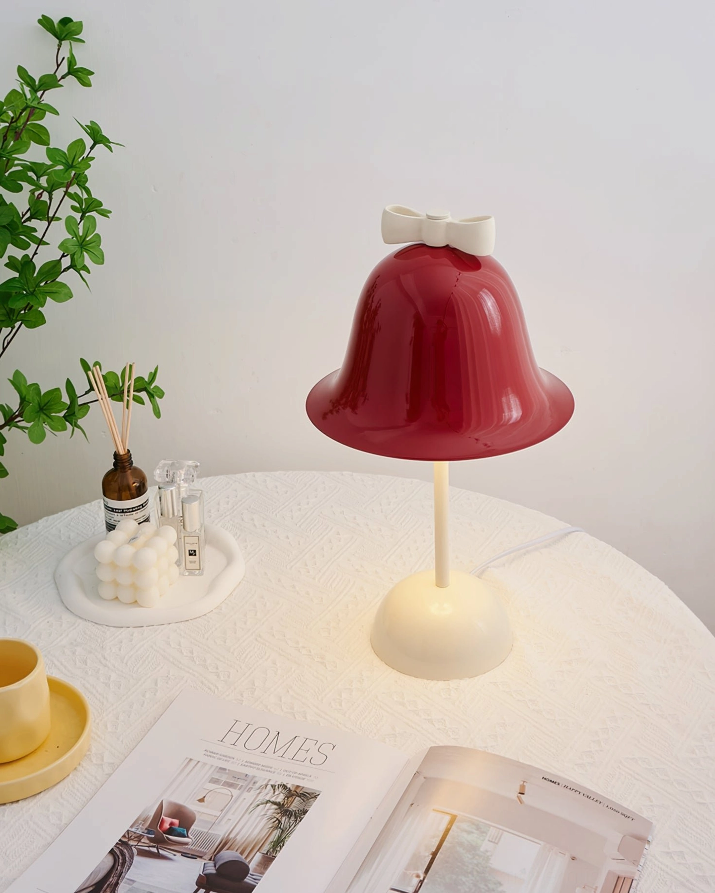 Bow Bell table lamp front view on white round table with matching home décor, diffuser, and interior design magazines