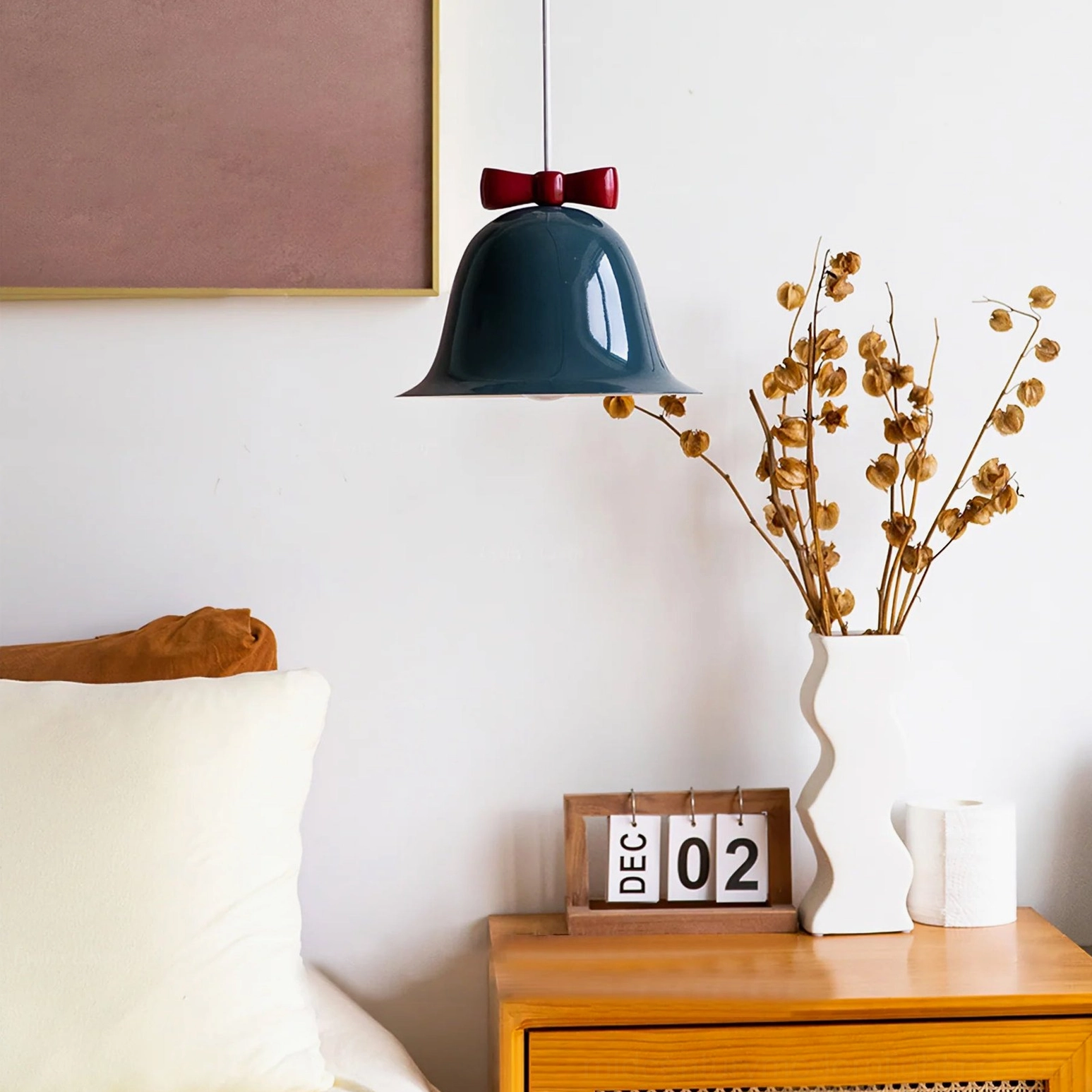Dark teal bow bell pendant lamp with red bow detail hanging over wooden bedside table
