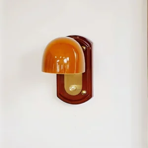 Close-up detail of Bradley wall lamp showing glossy amber dome shade, polished brass accents and minimalist wood mounting plate
