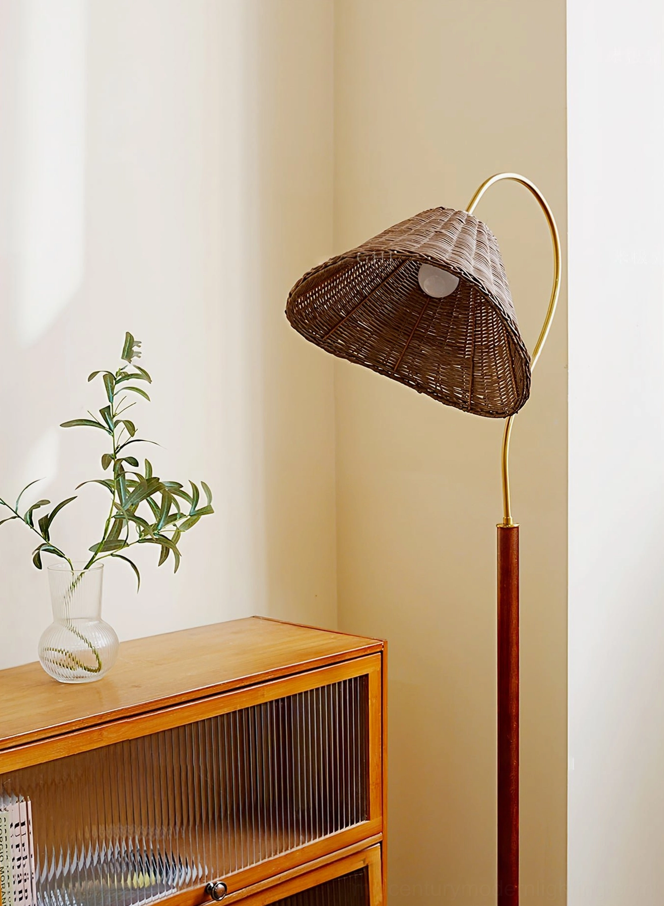 Side view of Brady floor lamp showing brass curved metal arm and rattan shade beside wooden cabinet, mid-century modern design details