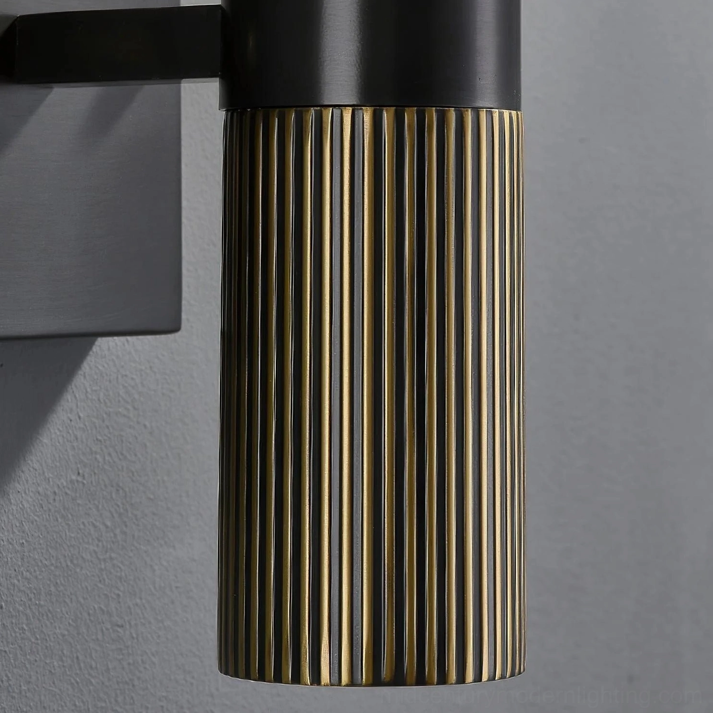Close-up side view of brass wall lamp base with fluted bronze finish and matte black mounting bracket