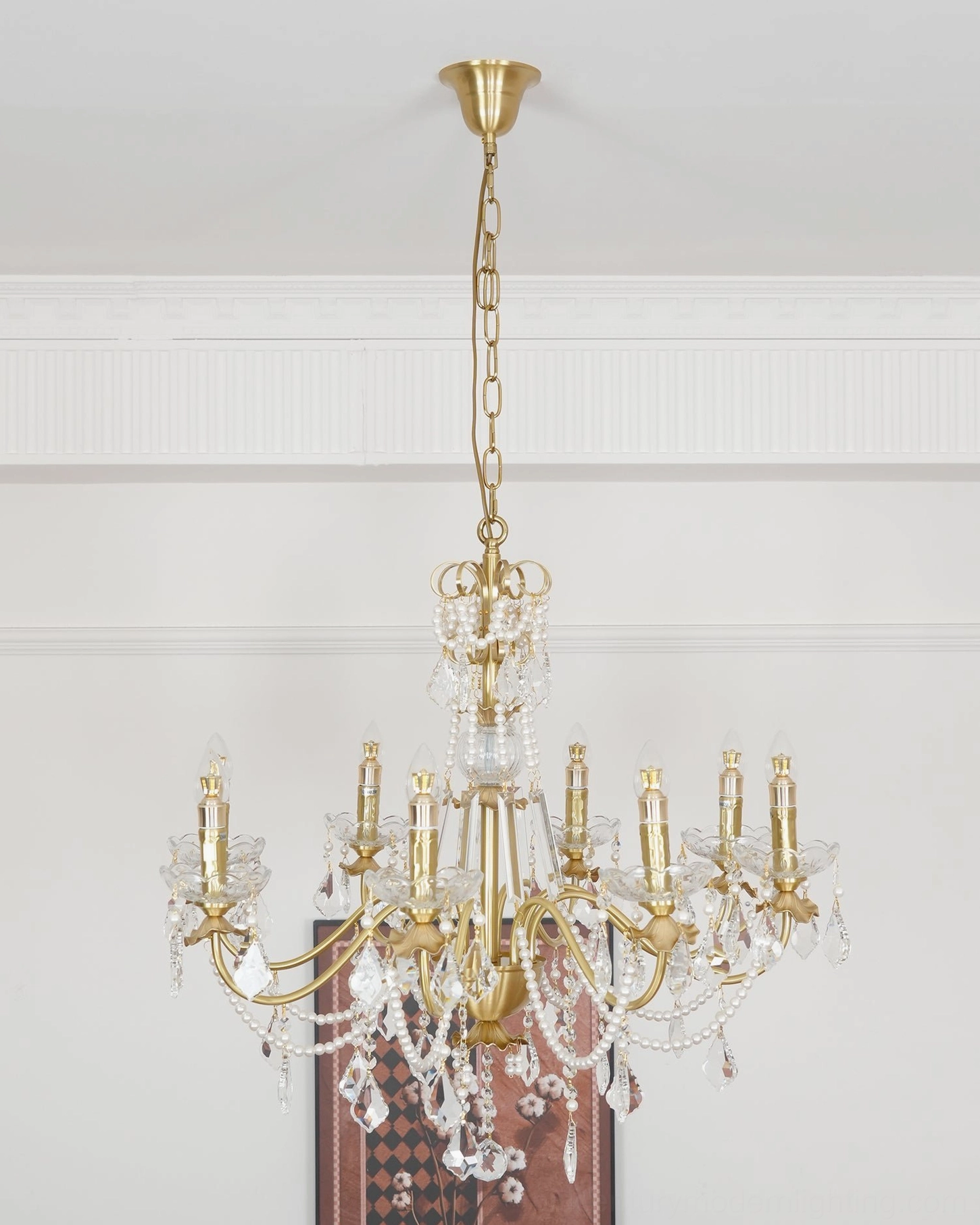 Polished brass chandelier with hanging crystal droplets and candle-style lamp sockets, low-angle room view