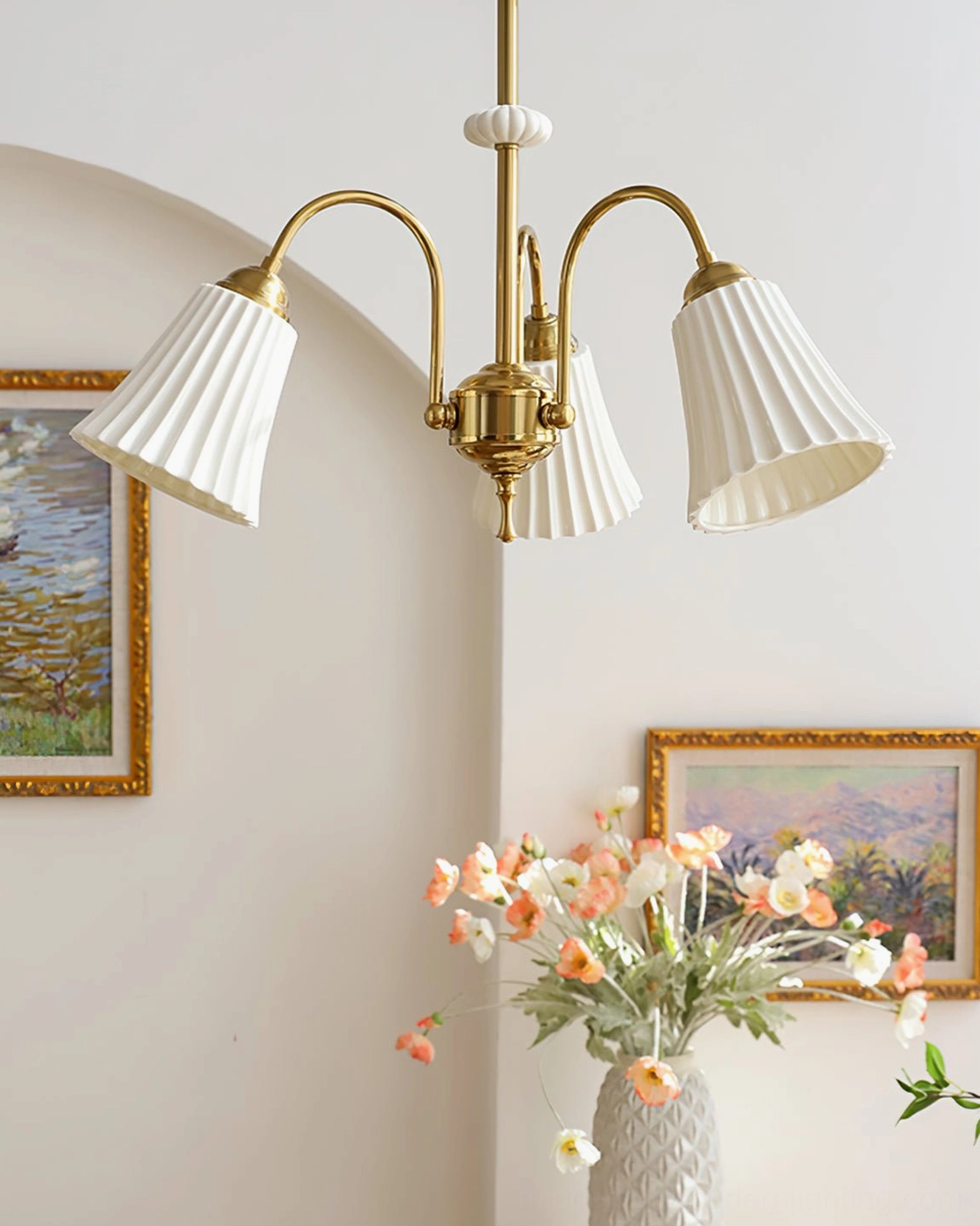 4-head brass chandelier with white pleated shades in vintage living corner featuring art paintings and decorative flower vase, French country style